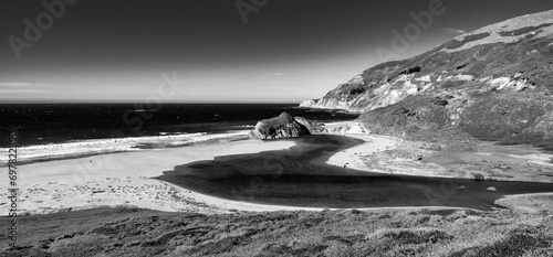 Dramatic image of the Little Sur River running and winding into the Pacific Ocean off of highway 1, California  with white sandy beach and waves.