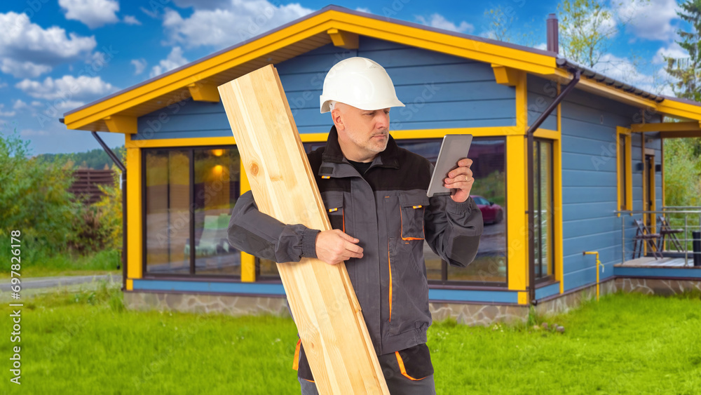 Man builder. Construction crew worker holds board. Builder with tablet near country house. Construction cottage. Engineer is holding electronic tablet. Man builder stands near finished house Man builder. Construction crew worker holds board. Builder with tablet near country house. Construction cottage. Engineer is holding electronic tablet. Man builder stands near finished house