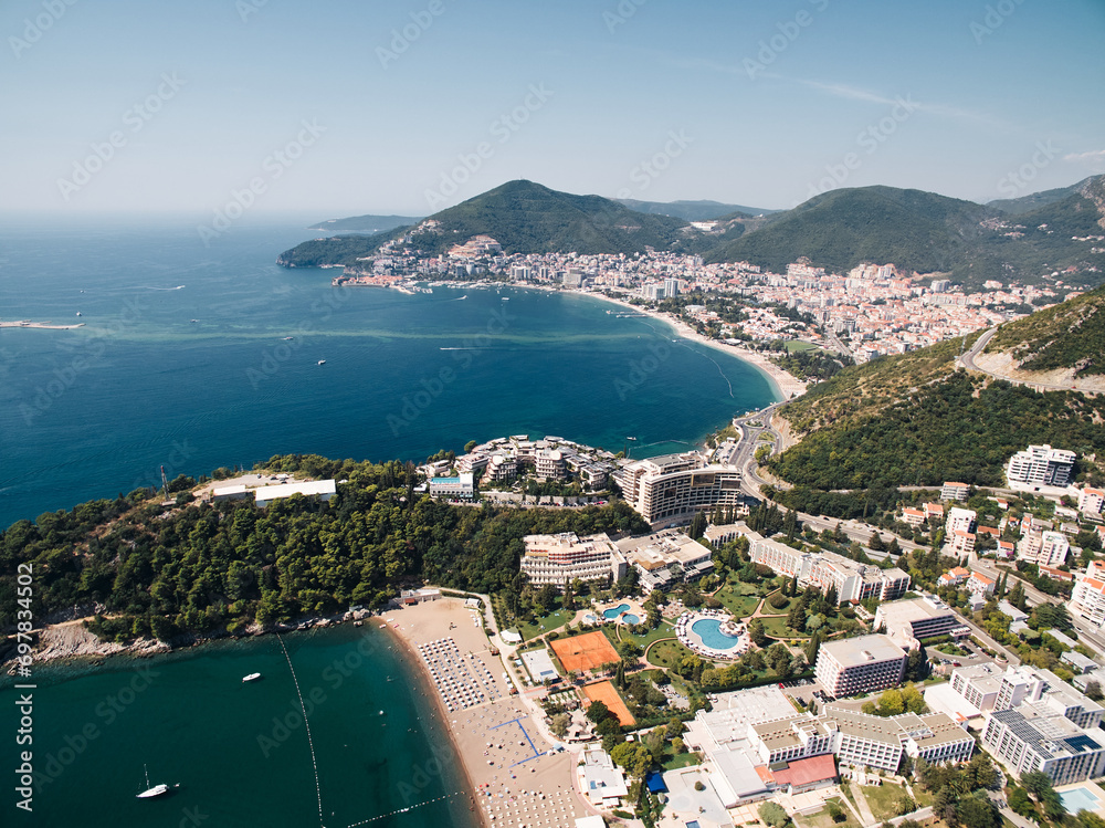 Sandy beach by the sea opposite hotels with swimming pools at the foot of the mountains. Budva, Montenegro. Drone