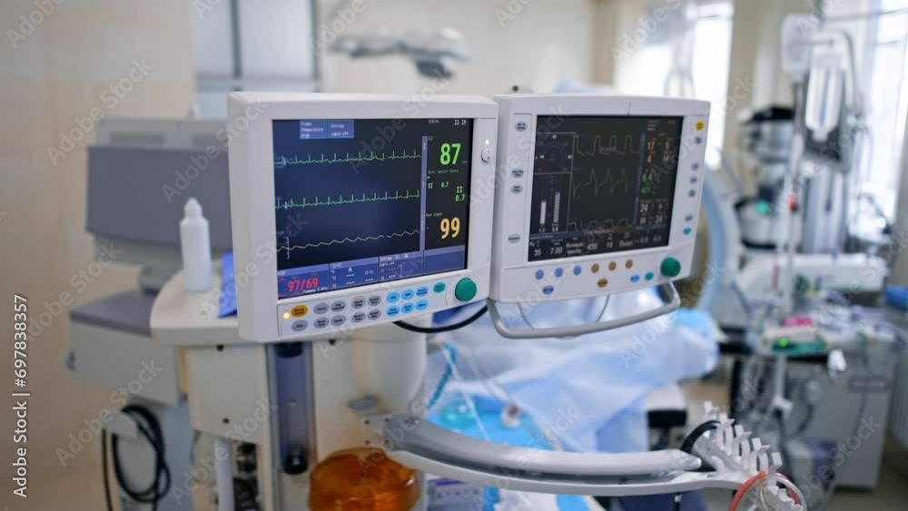 Monitors of lung ventilator machine displaying the life signs of a patient. Top vie won the modern surgery with a variety of equipment and surgeon working at backdrop. Monitors of lung ventilator machine displaying the life signs of a patient. Top vie won the modern surgery with a variety of equipment and surgeon working at backdrop.