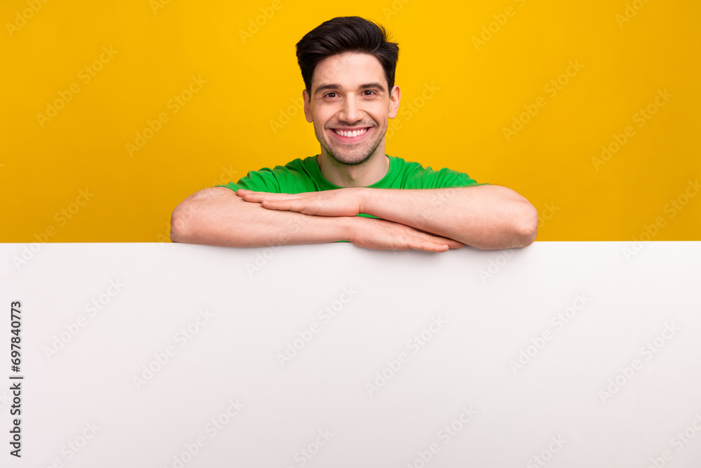 Photo of toothy beaming man with bristle dressed green t-shirt lean on white placard empty space isolated on yellow color background