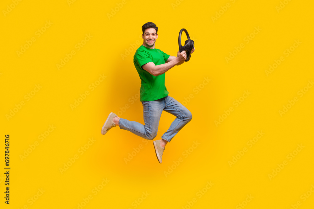 Full length photo of optimistic satisfied man jumping with steering wheel in hands at driwing lessons isolated on yellow color background