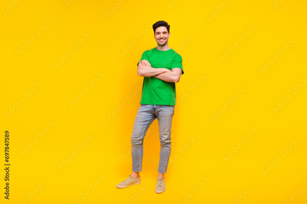 Full length photo of optimistic pleasant nice man dressed green t-shirt jeans holding arms crossed isolated on yellow color background