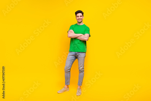 Full length photo of optimistic pleasant nice man dressed green t-shirt jeans holding arms crossed isolated on yellow color background
