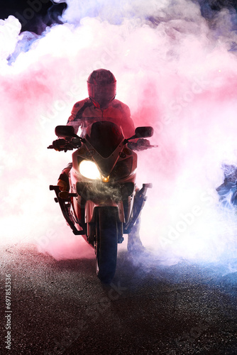 Motorcyclist in a leather jacket suit through the red and blue smoke on a motorcycle at night