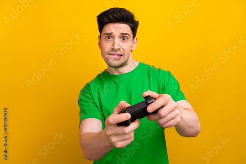 Photo portrait of attractive young brunet man play station nervous dressed stylish green clothes isolated on yellow color background © deagreez