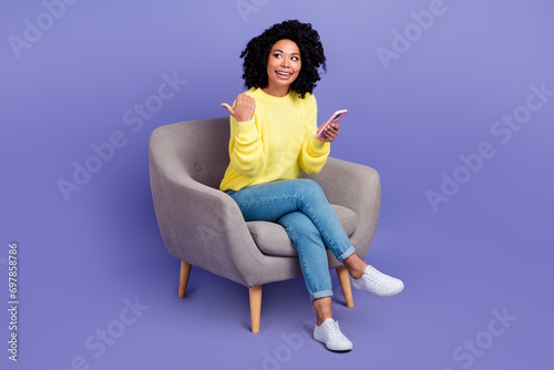 Full body photo of smart person wear knit pullover sit in armchair look directing at offer empty space isolated on purple color background