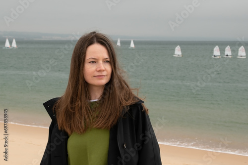 Beautiful young woman with long brown hair in a black coat on the beach.