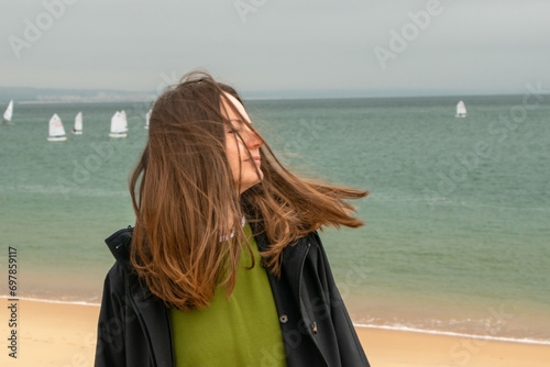 Young woman with windy hair on the beach with sailboats in the background