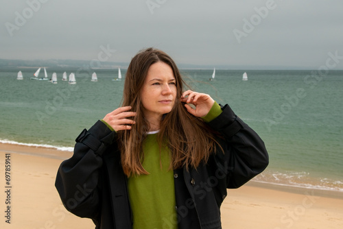 Portrait of a young woman on the beach. She is wearing a green jacket.
