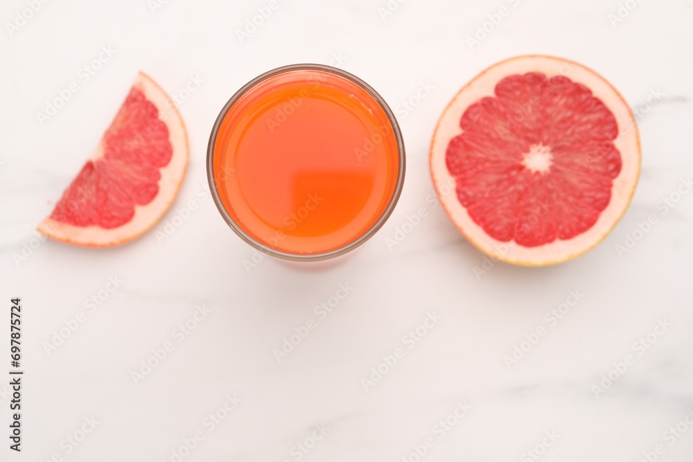 Tasty grapefruit juice in glass and slices of fresh fruit on white table, top view. Space for text Tasty grapefruit juice in glass and slices of fresh fruit on white table, top view. Space for text