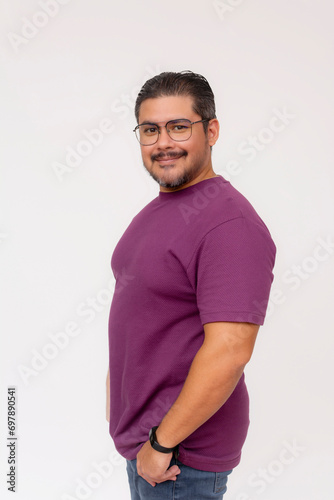 A friendly chubby man of mixed ancestry wearing glasses. Half body photo, quarter turn pose, wearing purple waffle shirt and jeans, isolated on a white background.