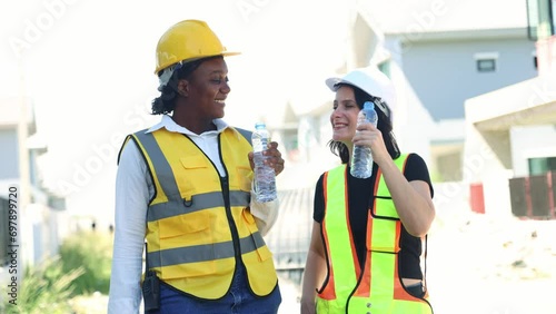 Architects and female workers construction site stand and drink clean distilled water in bottles to quench their thirst while refreshing themselves while smiling while taking breaks. photo