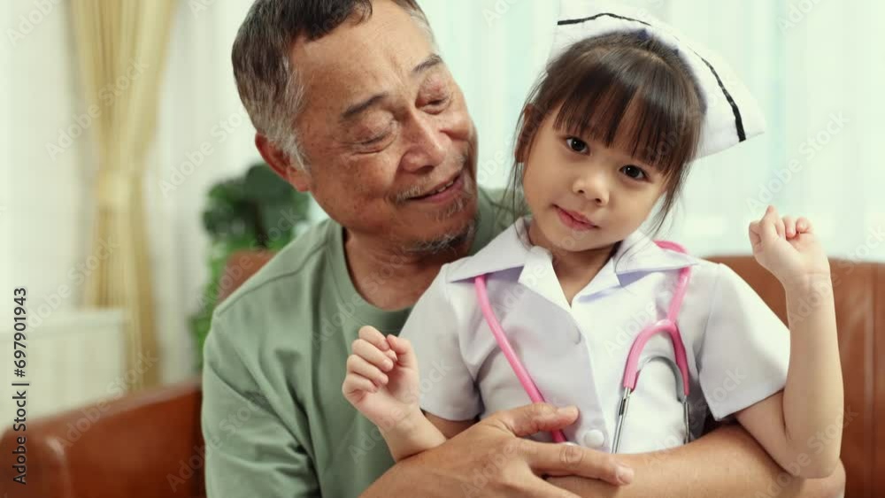 Retired grandfather in happy mental health is with his cute granddaughter dressed in a cute white nurse's uniform sitting on the sofa hugging with love and affection. Retired grandfather in happy mental health is with his cute granddaughter dressed in a cute white nurse's uniform sitting on the sofa hugging with love and affection.