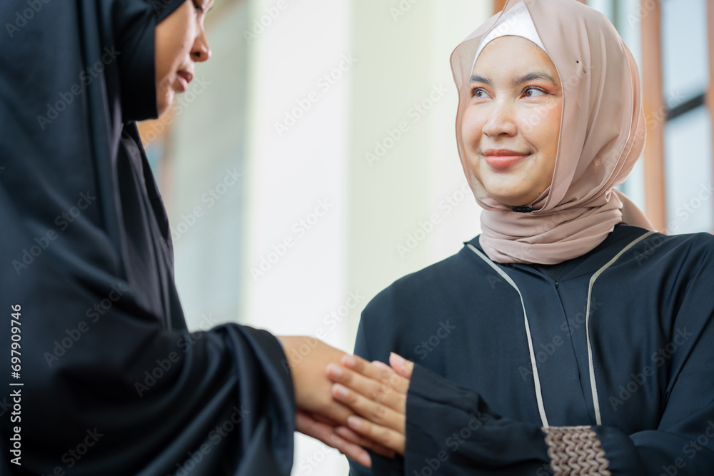 Φωτογραφία Two good-looking Asian Muslim women, hello, greeting, and Quran at the wooden table at his house during the night during the month of ramadan, Arabic calligraphy meaning Al Quran