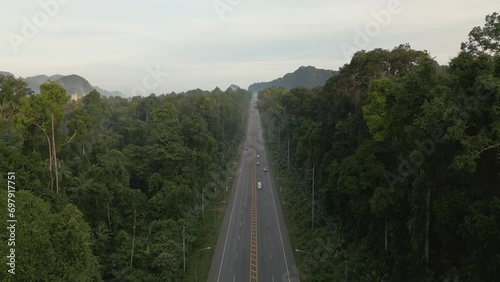 A video from a drone slowly flying from a long straight road with cars moving back and forth in the morning, gradually ascending until it reveals a distant view of forests, mountains, and mist in the 