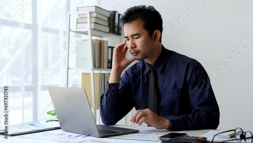 The tired young man feels eye strain, eyestrain from paperwork, and laptop, stress person for a long time, headaches, and eye problems from sitting at a desk in the office. Office syndrome concept. photo