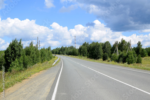 Empty highway surrounded by forest. Beautiful summer landscape, white clouds on a blue sky.
