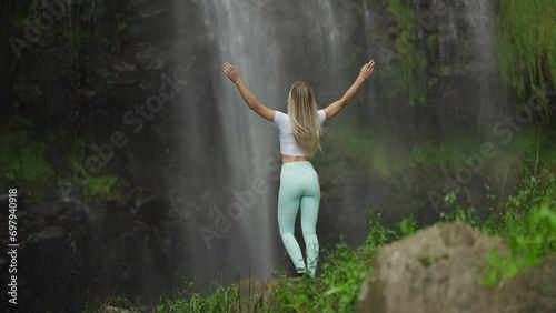 Wallpaper Mural Fit woman in sportive clothing reaching base of tropical waterfall throwing hands up Torontodigital.ca