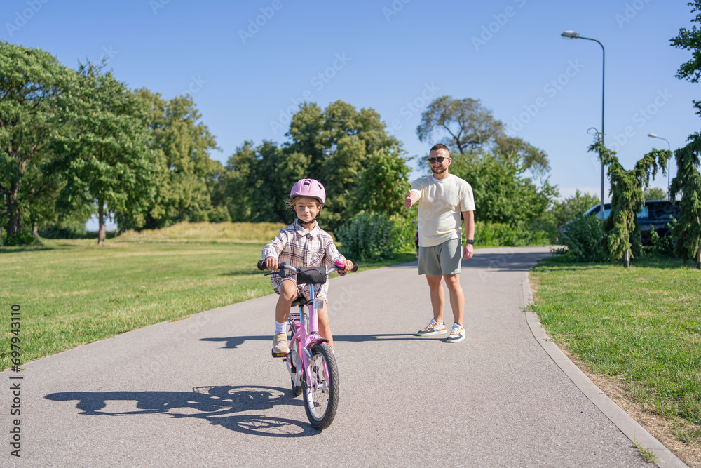Excited father teaching girl to ride a bike, summer fun and park outdoors. Happy kid, learning and riding bicycle with help from dad, parent and safety for healthy development.