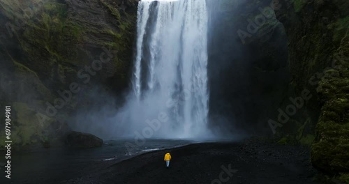 Man Wearing Yellow Jacket Walking Near Skogafoss Waterfall, Skoga River, South of Iceland. Slow Motion photo