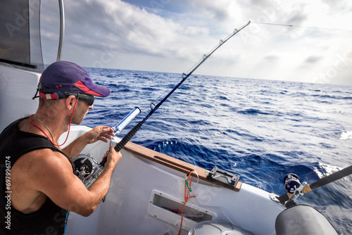 Tough man wearing baseball cap on board ship while fishing against blue sea background.