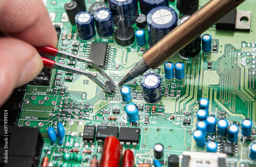 Close up of a technician's hands in a workshop. Repairer is soldering circuit board of electronic device on table with tweezers.