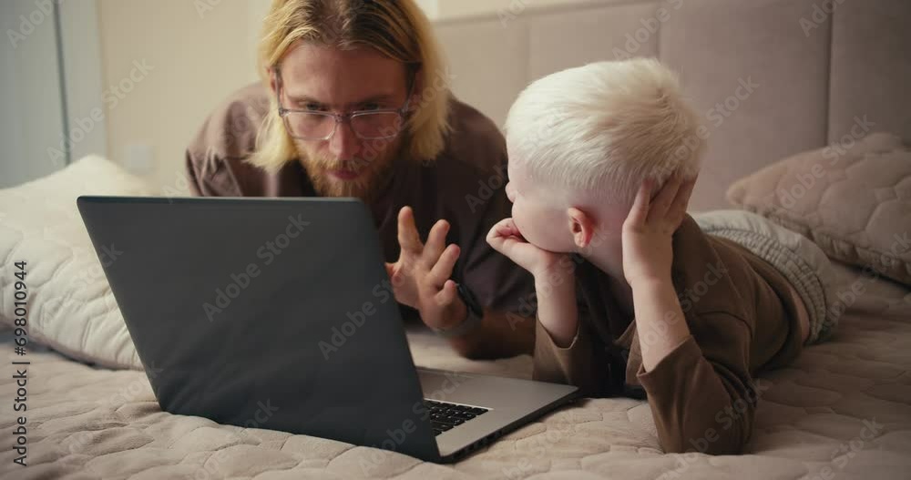 A happy albino boy with white hair looks at his father while watching an educational film and asks him a question. The man answers his boy and tries to clarify all his questions