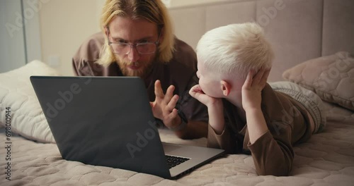 A happy albino boy with white hair looks at his father while watching an educational film and asks him a question. The man answers his boy and tries to clarify all his questions photo