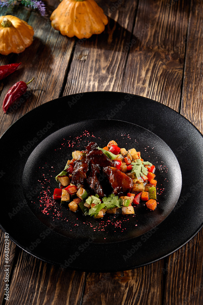 Braised beef cheeks with a vibrant vegetable ratatouille, served on a rustic black plate, autumn harvest-inspired