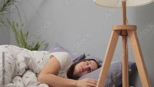 Young adult cheerful woman going to sleep shutting off nightlamp turning off electric light rubbing her eyes feeling sleepless lying in bed in the evening photo