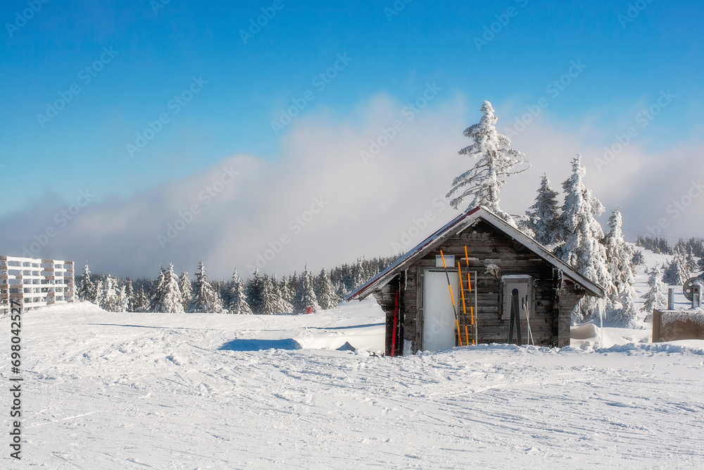 Vacation rural winter background landscape with small wooden alpine house covered with snow, ski slope