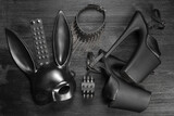 Black rabbit mask, studded leather bracelets, high heels shoes and neck choker on the black wooden flat lay table background.