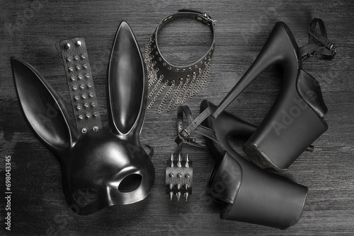 Black rabbit mask, studded leather bracelets, high heels shoes and neck choker on the black wooden flat lay table background. photo