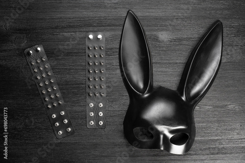 Black rabbit mask and studded leather bracelets on the black wooden table flat lay background.