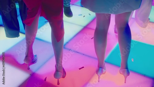 Slender female legs in high-heeled shoes dance on luminous square disco floor. Vintage disco party with dancing girls. Party at nightclub in style of 80s. Beautiful colored flashing floor in nightclub