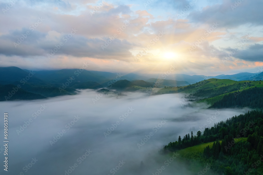 Fog envelops the mountain forest. The rays of the rising sun break through the fog. drone view.