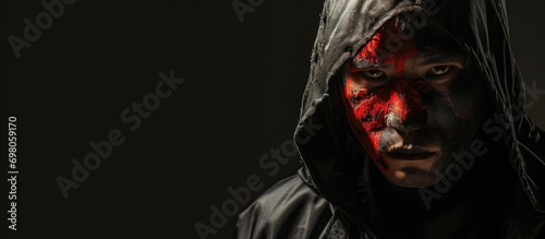 A menacing man with a Chinese flag on his face, in a dark hood with sharp shadows on a black backdrop. Copy space.