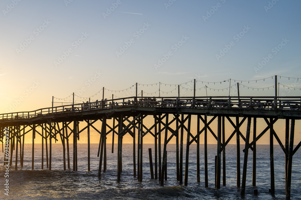 Serene dawn at Carolina Beach with a rustic pier stretching into the calm ocean against a pastel sunrise sky.