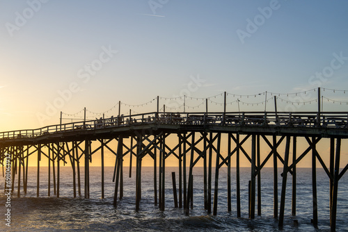 Serene dawn at Carolina Beach with a rustic pier stretching into the calm ocean against a pastel sunrise sky.
