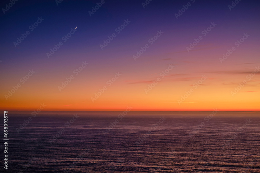 Serene summer sunset over sea waters and crescent moon in the sky.