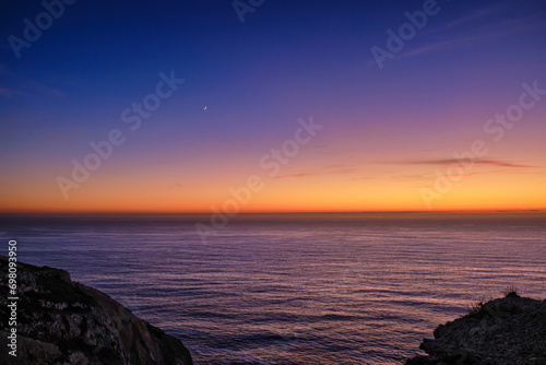 Obraz na płótnie Sunset over sea waters, dark cliffs and crescent moon in the sky. w salonie