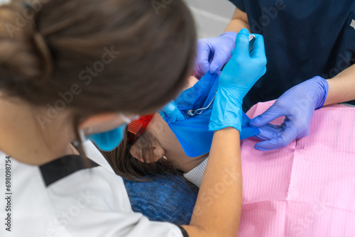 Process of installing a dental cofferdam for dental treatment on the jaw of a young woman wearing protective glasses in dentistry. Dentist uses a dental dam to isolate the tooth photo