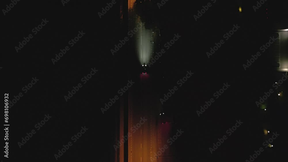 Aerial top down view following a car in a street during the night in Lugano, Switzerland. Cinematic drone shot over night city. Car headlights light up the road.