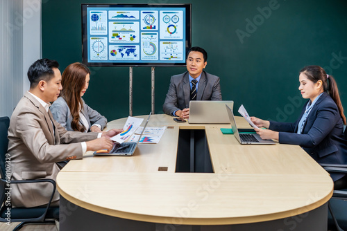 Smiling asian businessman boss executive talking to business people colleagues or partners sitting at conference table, male leader discussing work at team meeting or conversation with clients