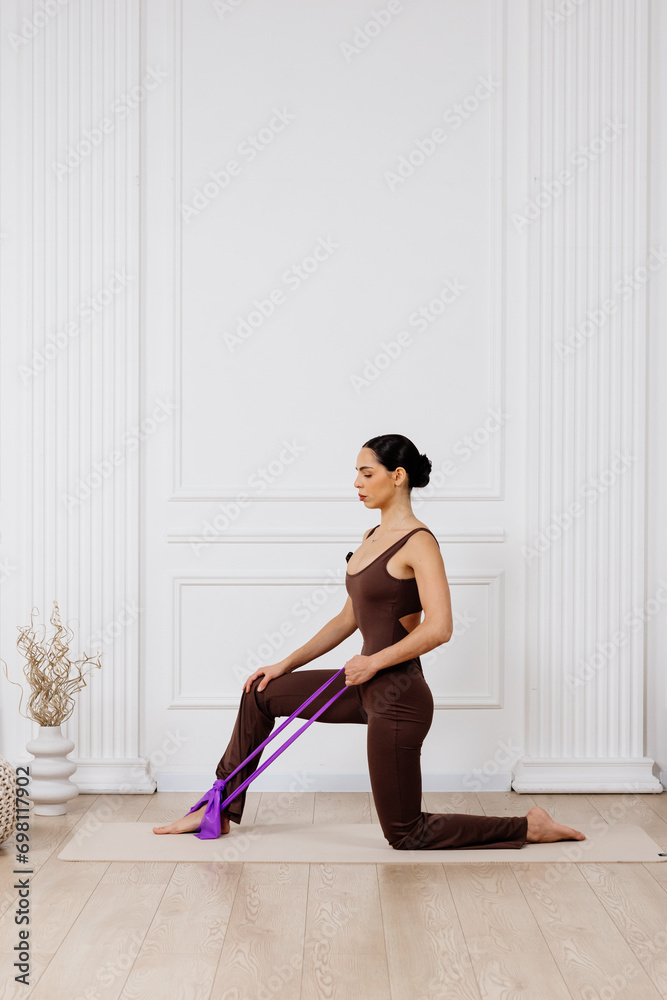 Fototapeta premium Athletic, beautiful woman doing exercises with a fitness elastic on a white background. Concept of sports equipment, healthy body and stylish fashionable clothes