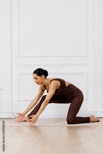 A woman wears dark sportswear, practices asana, and sports exercises for a flexible body. Training for beginners. Concept of sportswear and flexible healthy body.