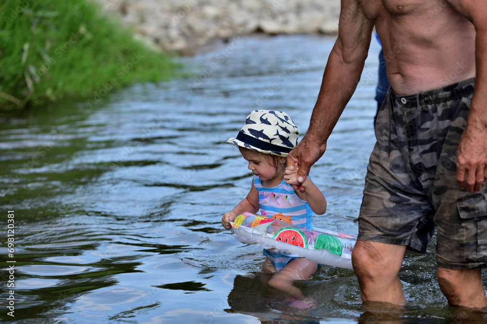 A grandfather teaches his granddaughter to swim in the river using an inflatable lifeline