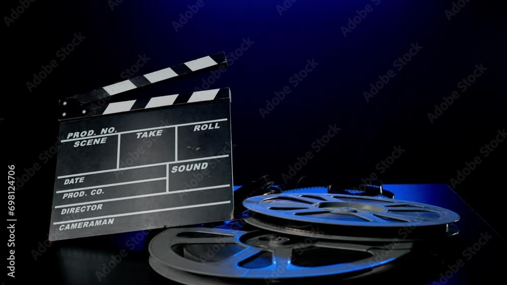 A clapper board and a reel of film roll on a wooden table . Film industry inventory in studio on black background in blue neon light.
