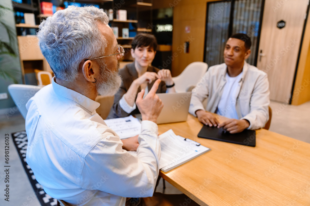 Obraz premium Group of mixed age colleagues discussing business issues during meeting in conference room